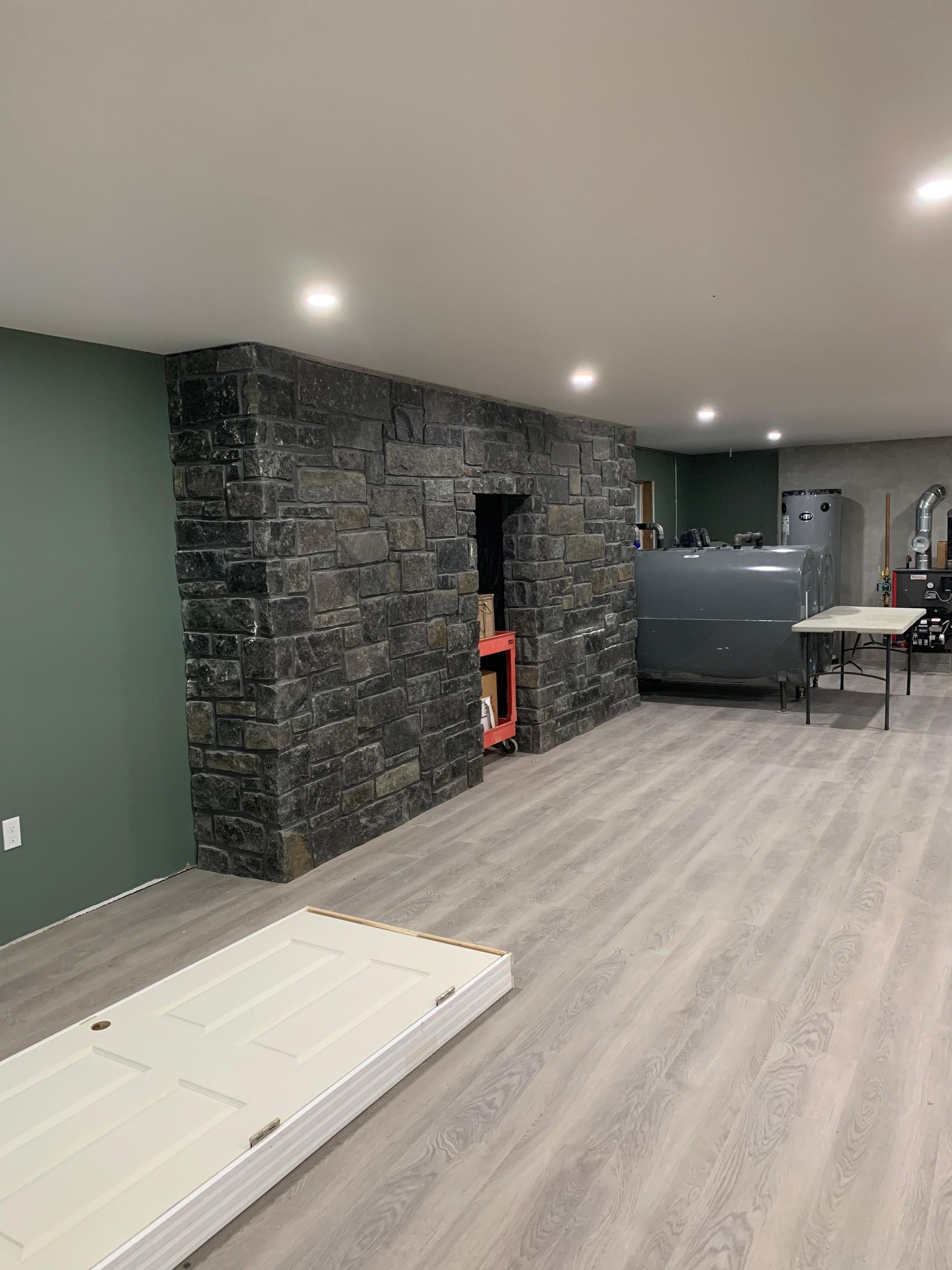 Basement with stone accent wall, green wall, gray flooring, recessed lighting, and a fuel tank.