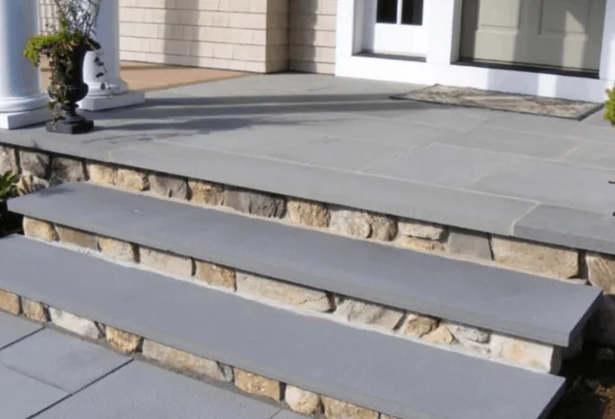 Stone steps leading to a building's entrance. Gray stone treads, and rock-faced risers.