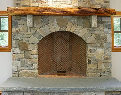 Stone fireplace with archway, herringbone interior, wooden mantel, and gray hearth.