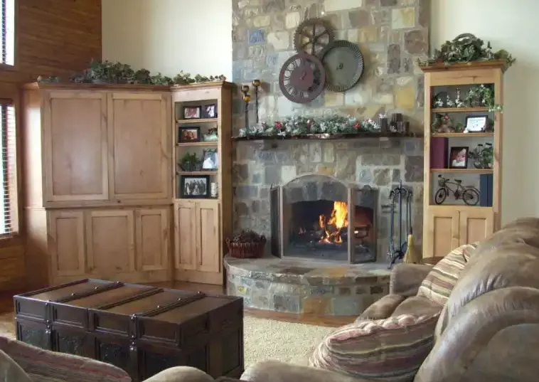 Cozy living room with fireplace, stone wall, built-in wooden shelves, and a brown leather trunk.