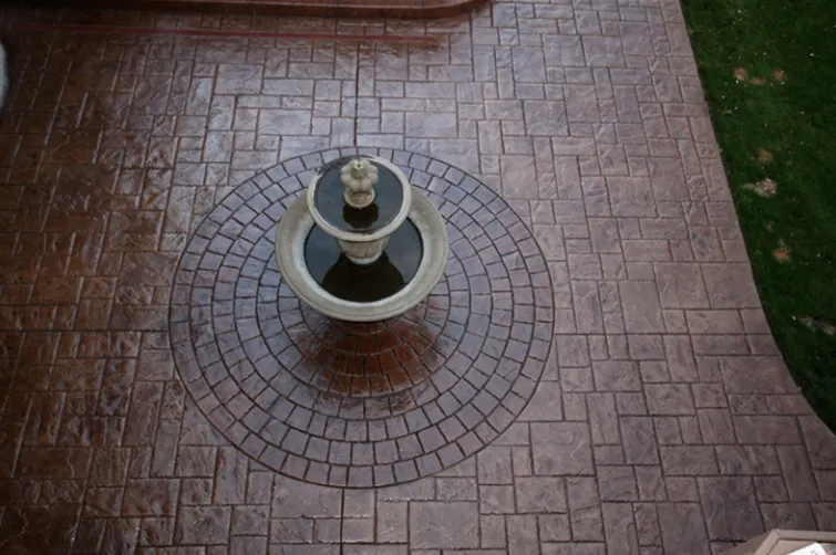 Stamped concrete patio with a fountain in the center. The patio is brown with a brick-like pattern.