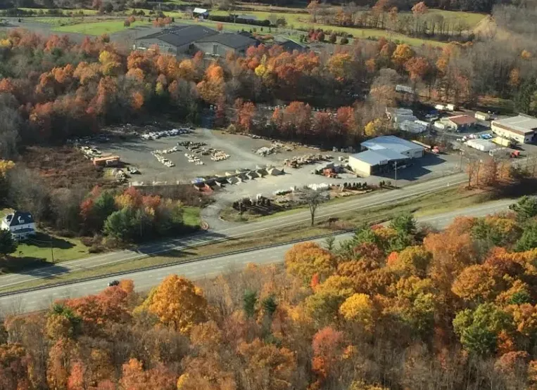 Aerial view of a business lot with equipment, surrounded by colorful autumn trees and a highway.