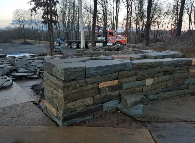 Stone wall under construction with a truck in the background. Construction site.