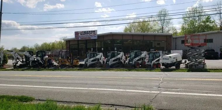 Heavy machinery showroom, with various construction vehicles parked in front. Building and road in background.