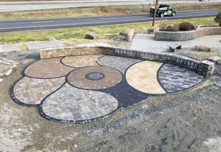 Multi-colored brick patio with curved walls and circular patterns, near a road.