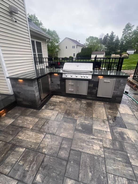 Outdoor kitchen with grill, fridge, and storage, built on a stone patio.