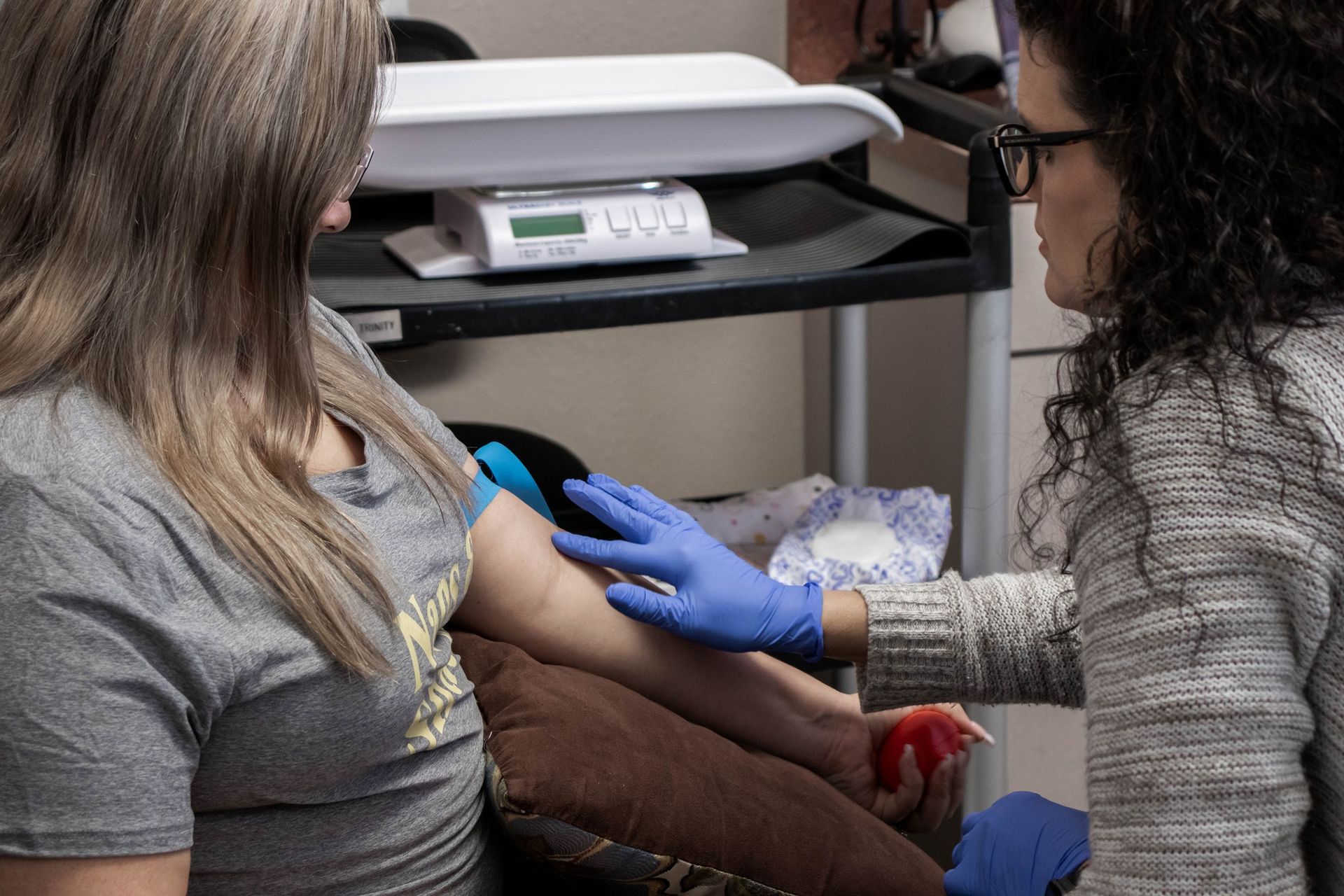 A healthcare worker wearing blue gloves prepares a patient's arm for a blood draw in a medical office setting.