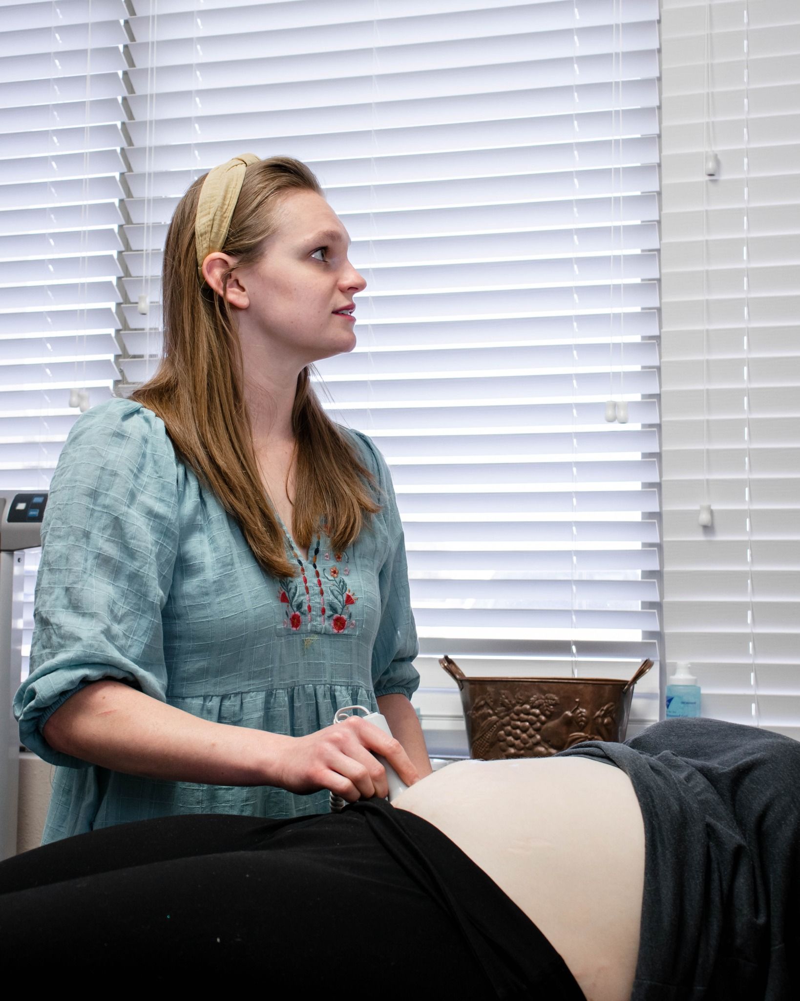 A person performing an ultrasound on another person's abdomen in a brightly lit medical room.