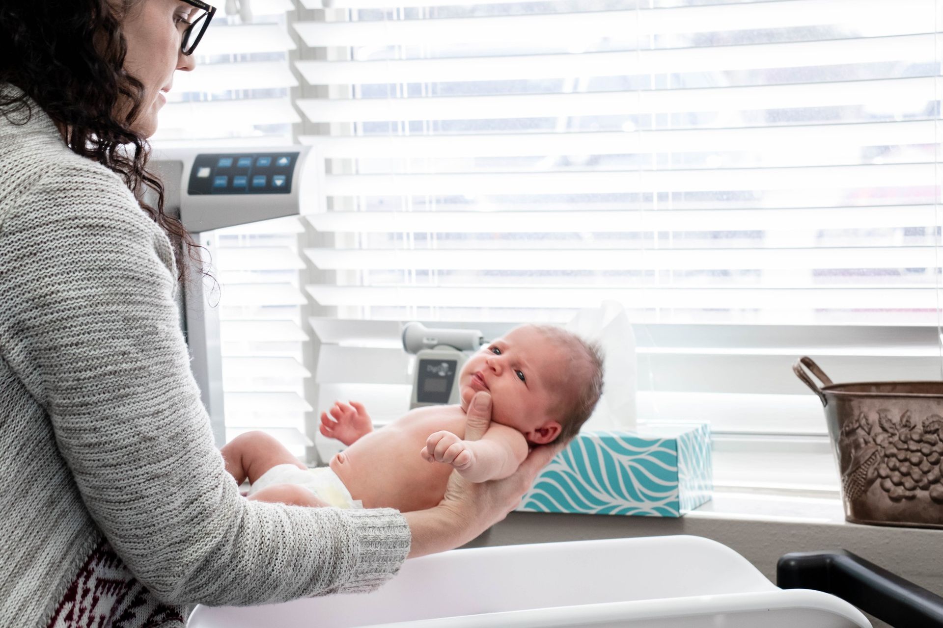 A person holds a newborn baby over a changing table in a brightly lit room.