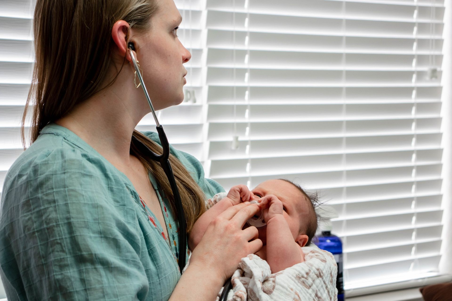 A person holds a baby wrapped in a blanket while using a stethoscope to listen to the infant's heart.