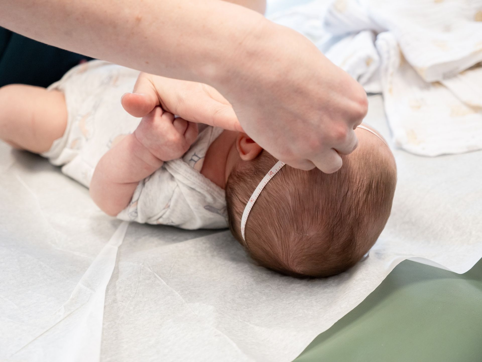 A person gently adjusting a thin, white headband on a baby lying on a white medical examination paper.