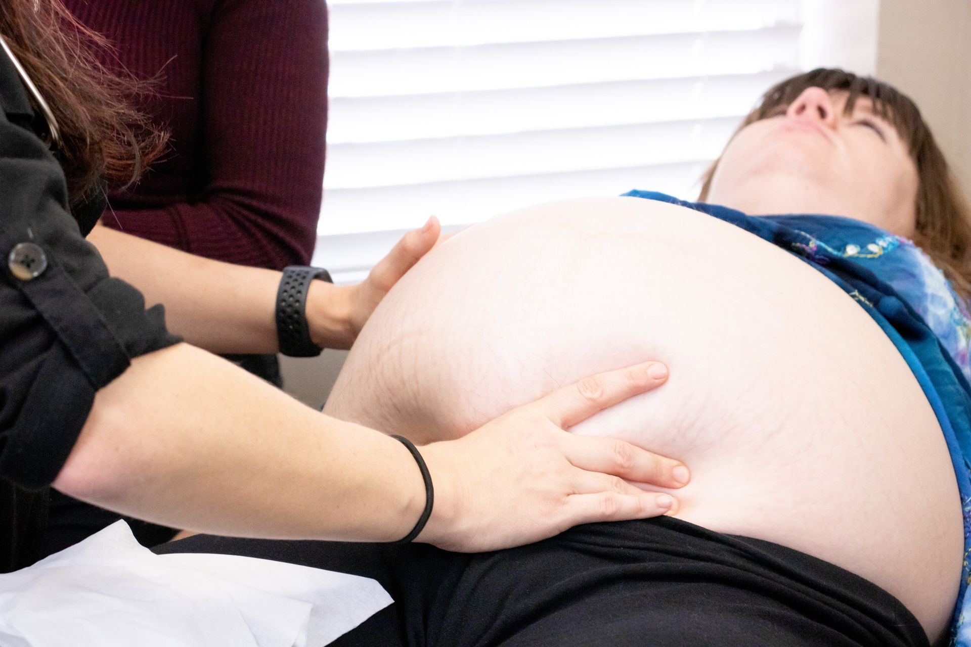 A medical professional examines a pregnant patient's abdomen during a prenatal appointment.
