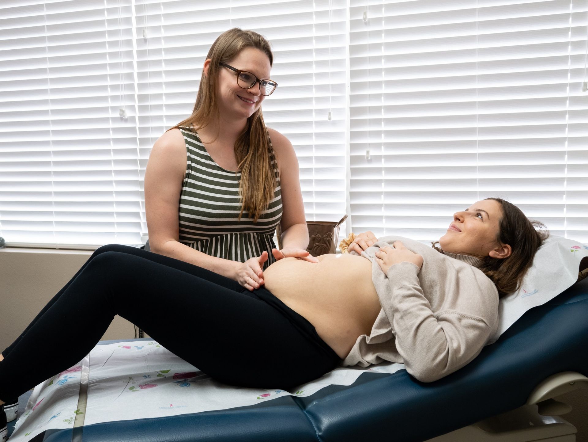 A midwife performs a prenatal abdominal exam on a patient lying on an exam table in a clinical setting.