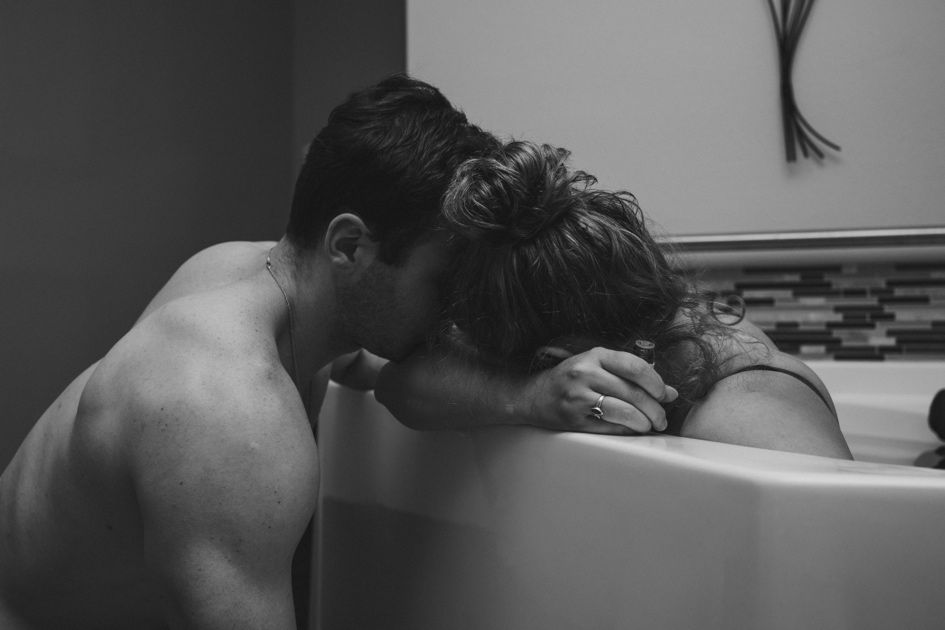 Person leans over a bathtub, comforting someone with their head resting on folded arms.