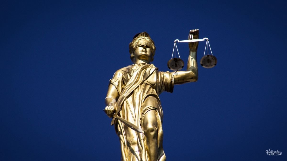 A golden statue of Lady Justice holding scales against a deep blue sky.