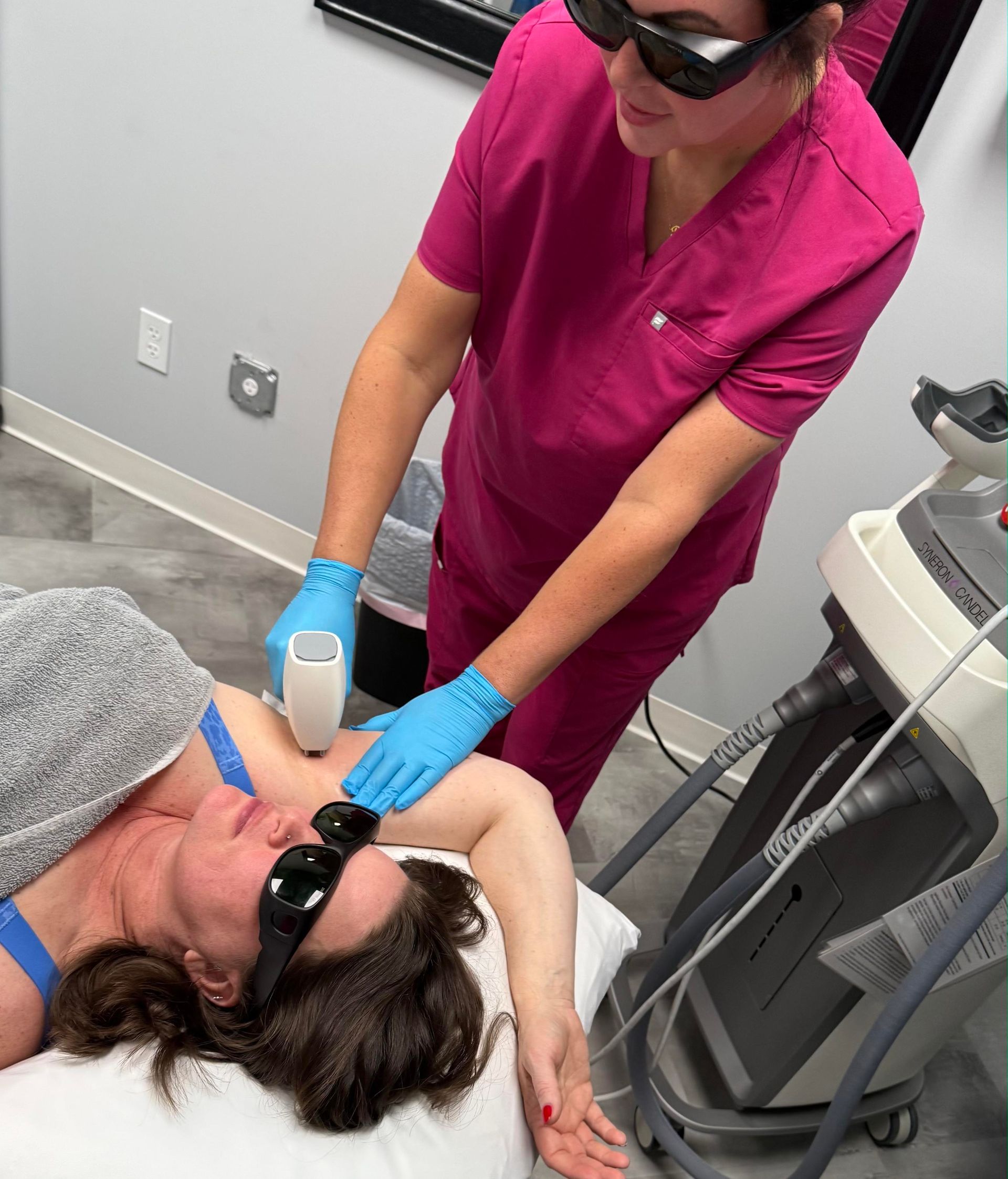 Healthcare worker in pink scrubs using an ultrasound probe on a patient wearing sunglasses.