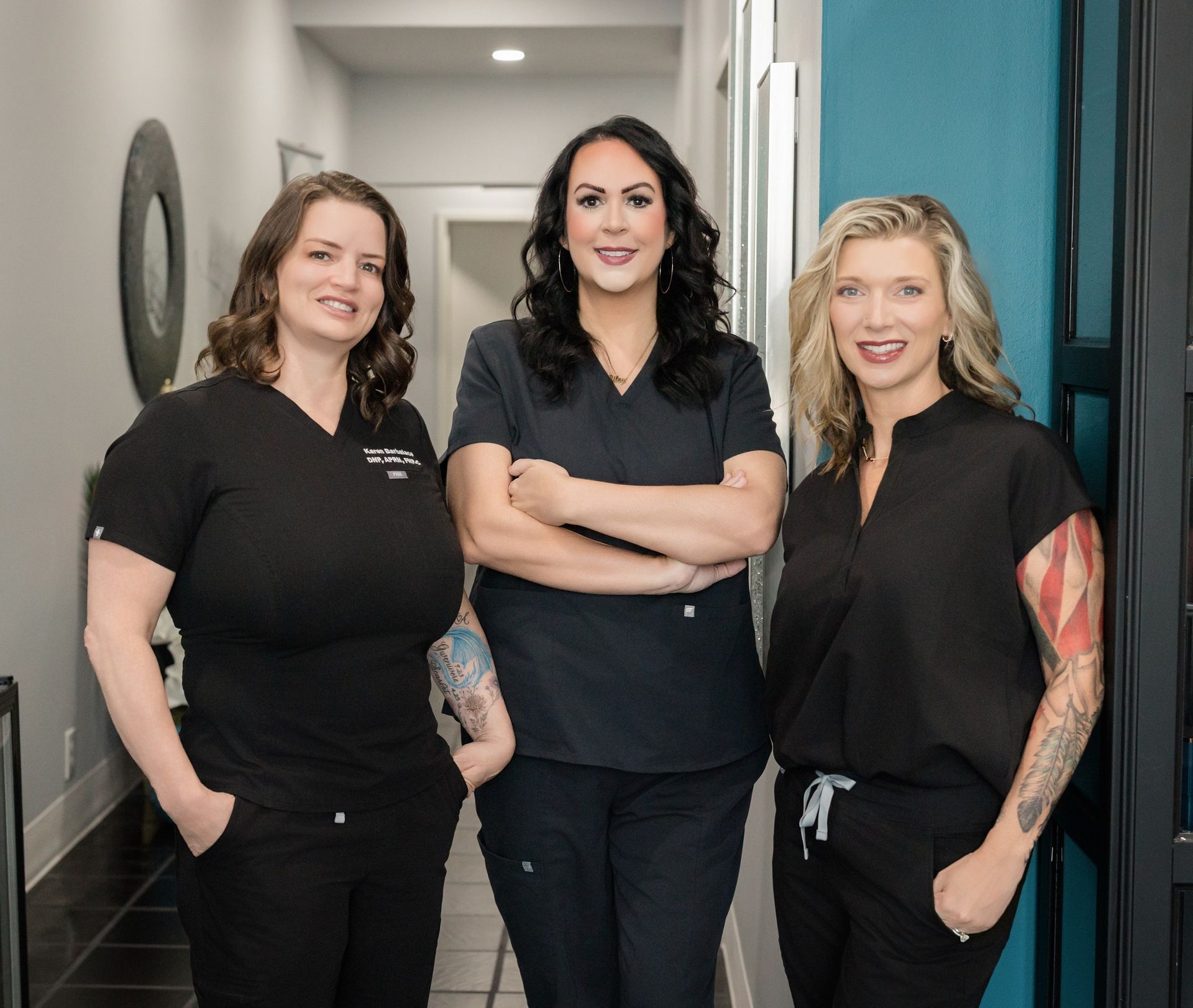 Three staff members in black uniforms standing together in a hallway, smiling at the camera.