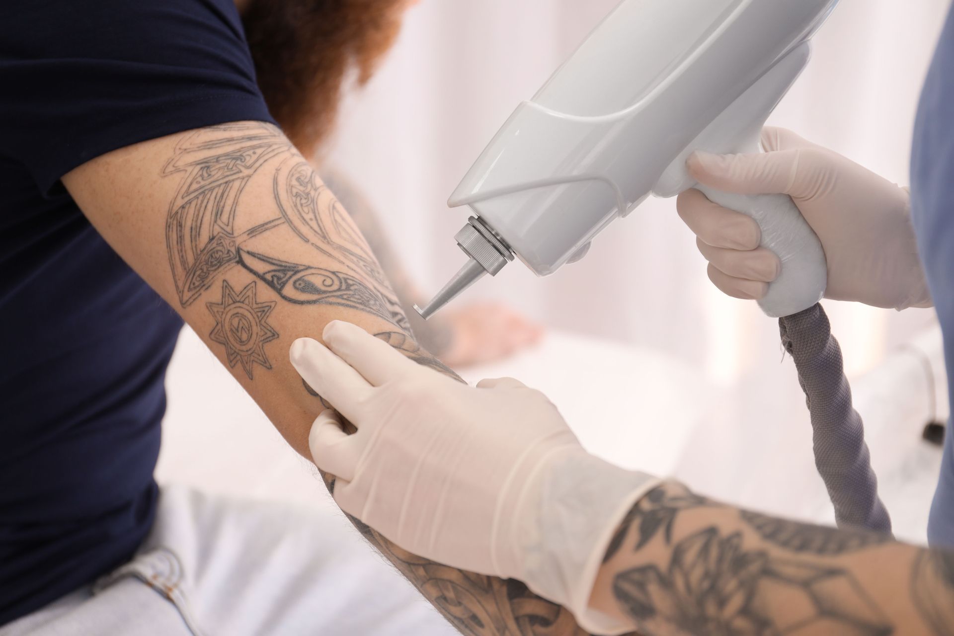 Tattoo artist using a machine to tattoo a client’s forearm while wearing gloves