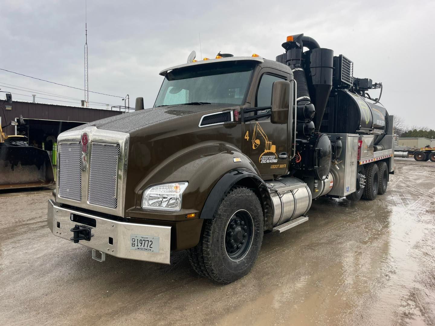 Brown vacuum truck on a gray concrete surface, with a tall black tank and multiple tires.