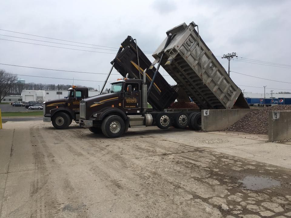 Two black dump trucks unloading gravel at a commercial site.