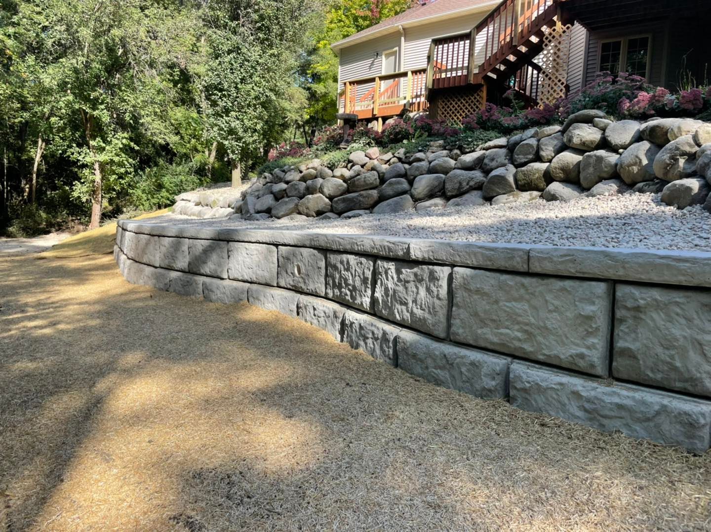 Stone retaining wall with gravel in front, house with deck in background.
