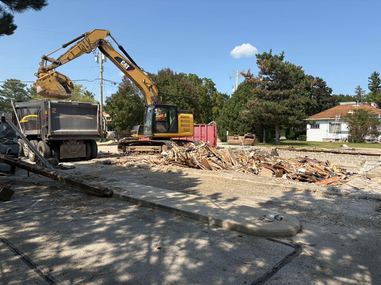 Yellow excavator loading debris into a dump truck at a construction site on a sunny day.