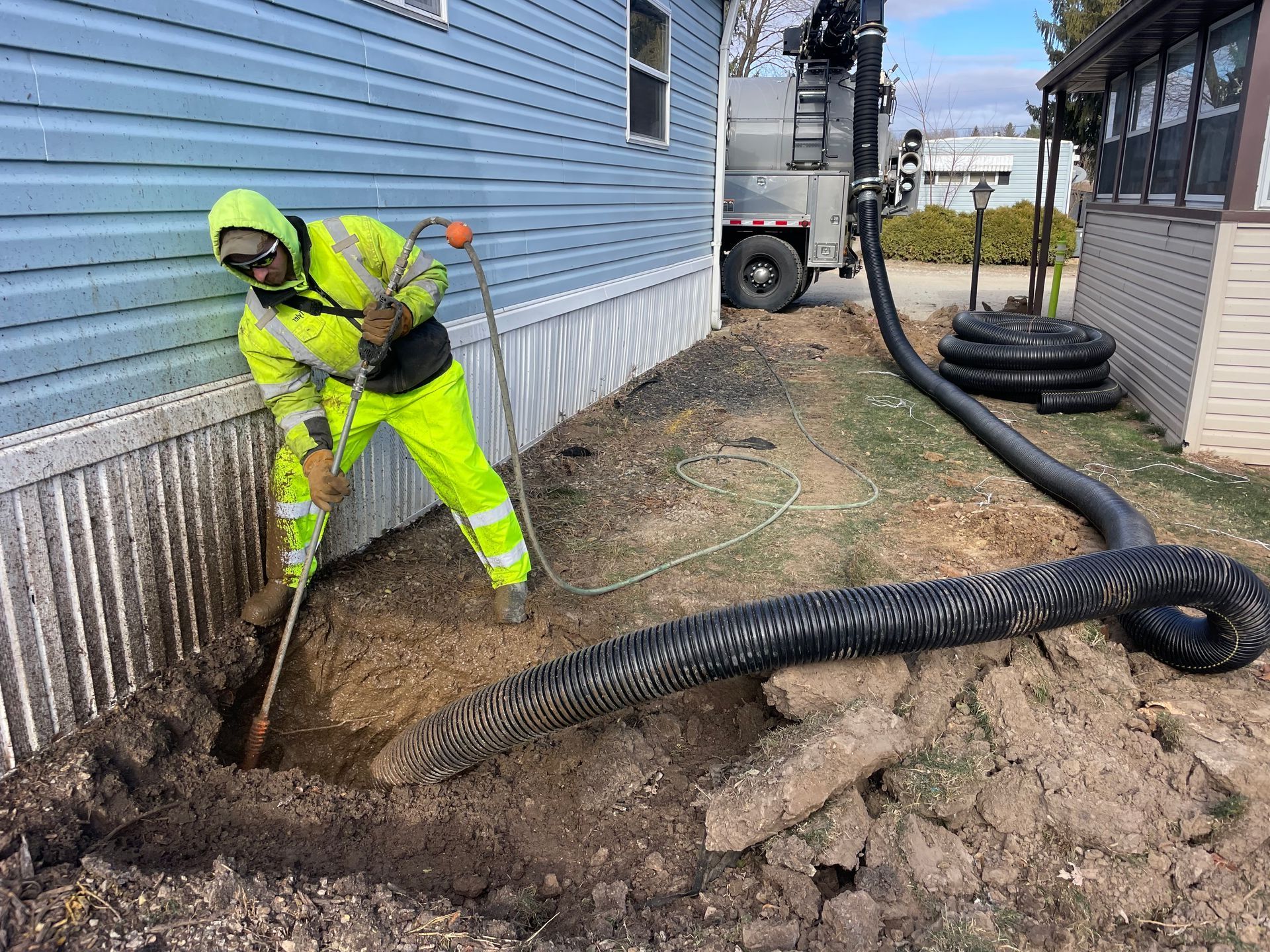 Worker in yellow digging next to a house with a black pipe connected to a truck.