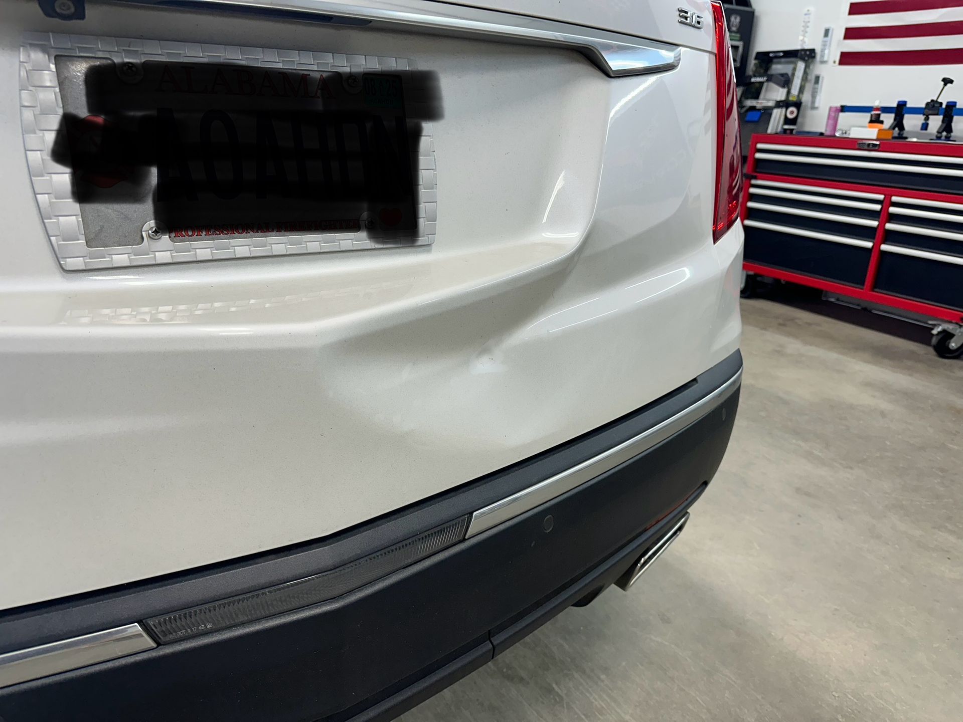 A white car with a damaged bumper is parked in a garage.