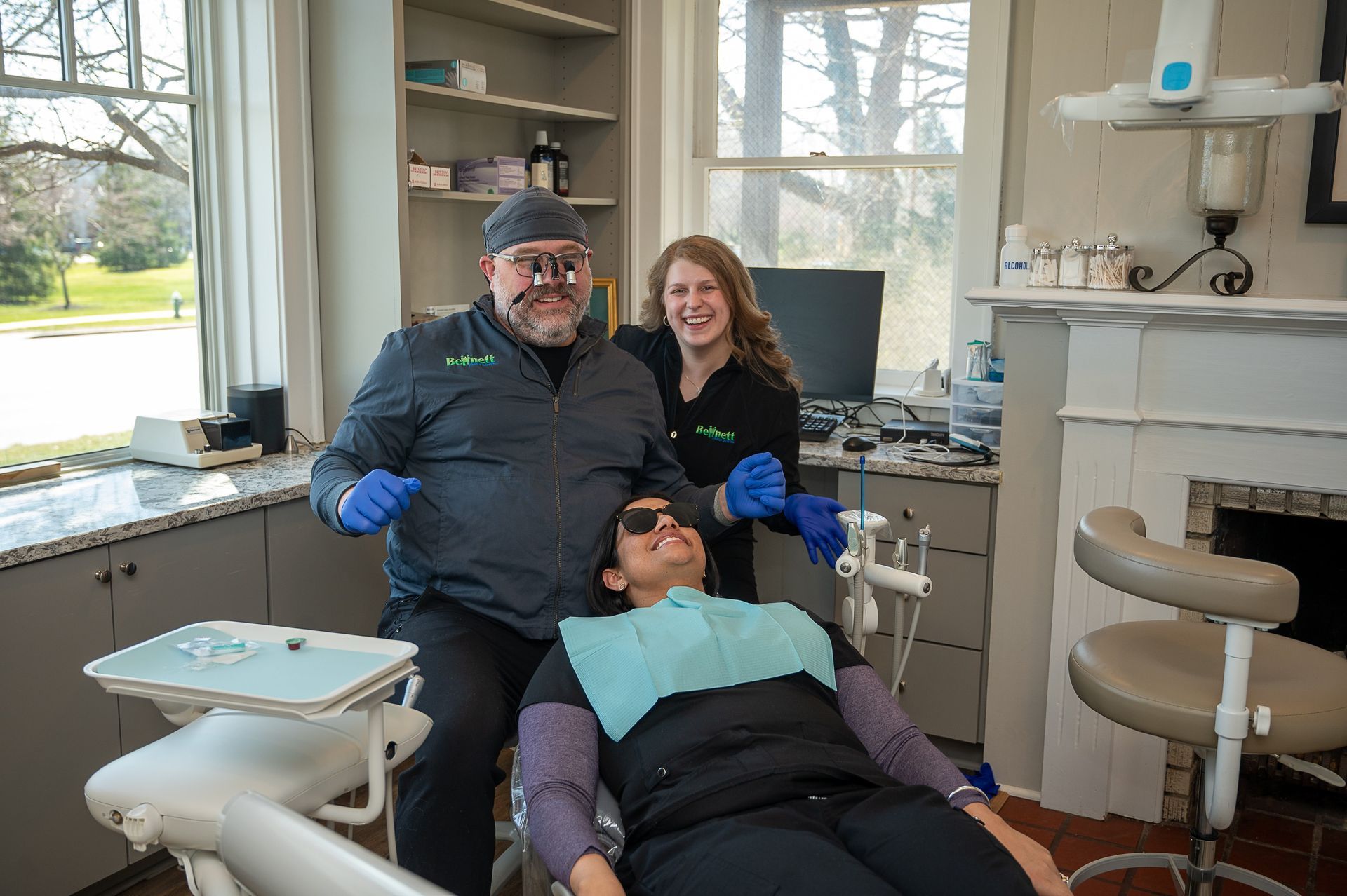 A man and a woman are standing next to a woman in a dental chair