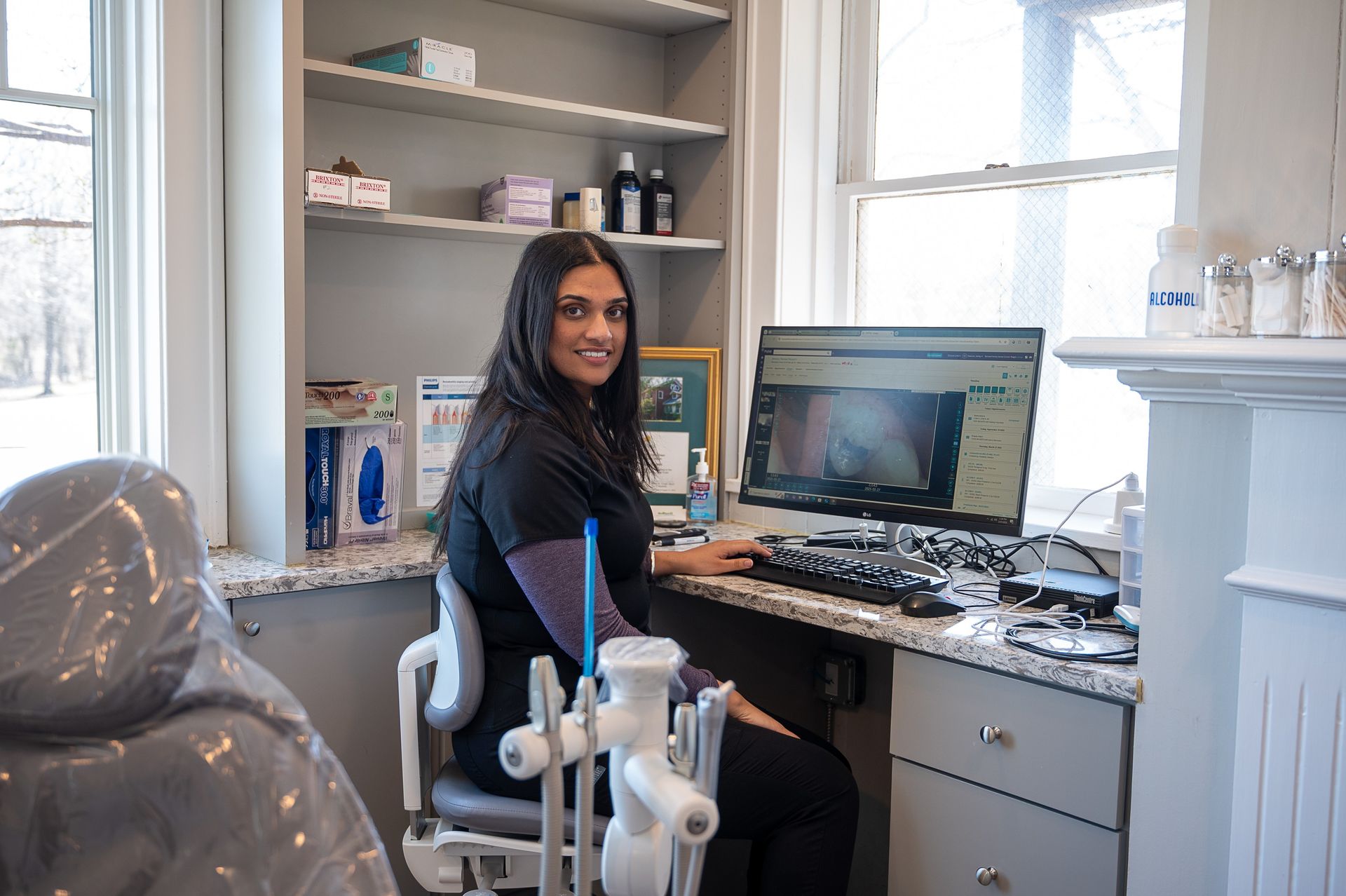 A woman is sitting in a dental chair in front of a computer