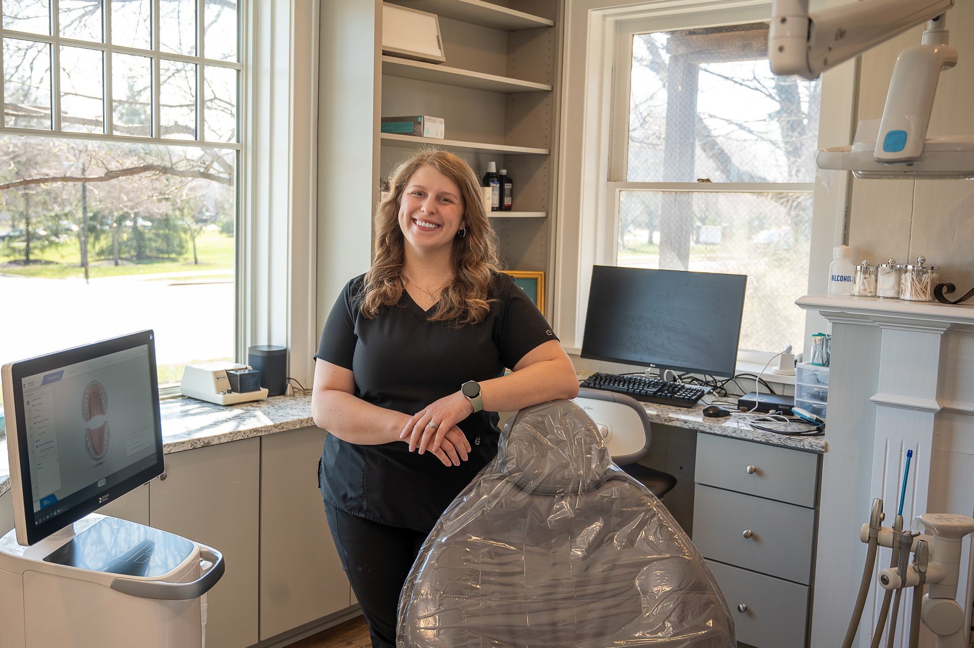 A woman is standing in a dental office next to a dental chair