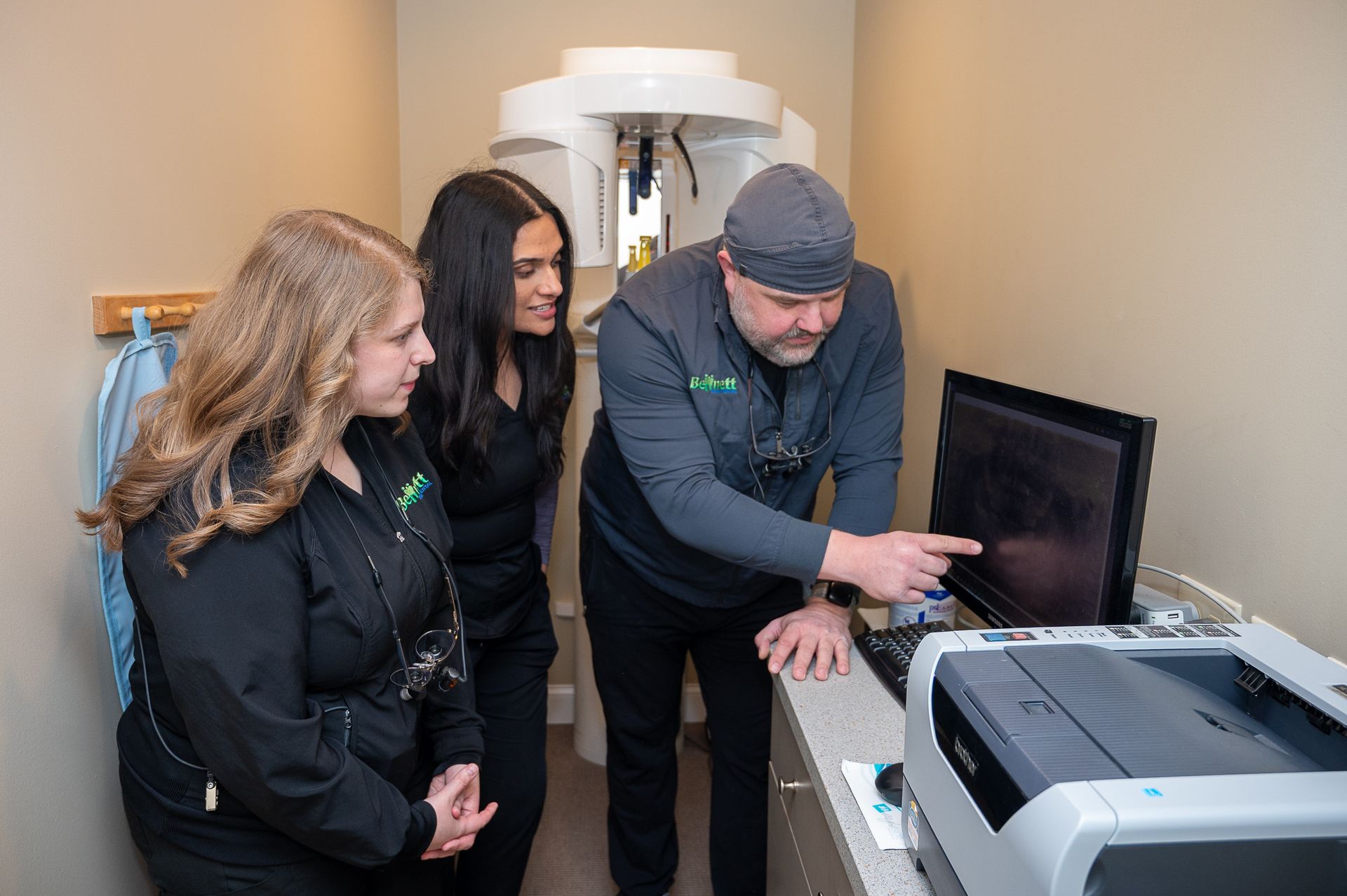 A man is pointing at a computer screen while two women look on