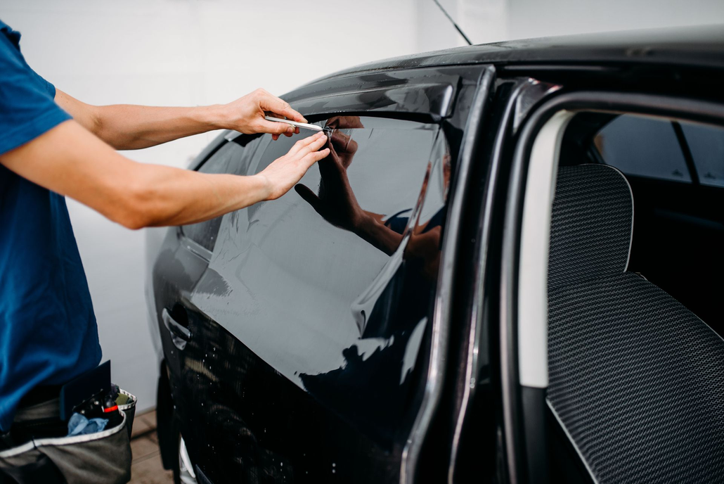 Person applying dark window tint to a black car door.