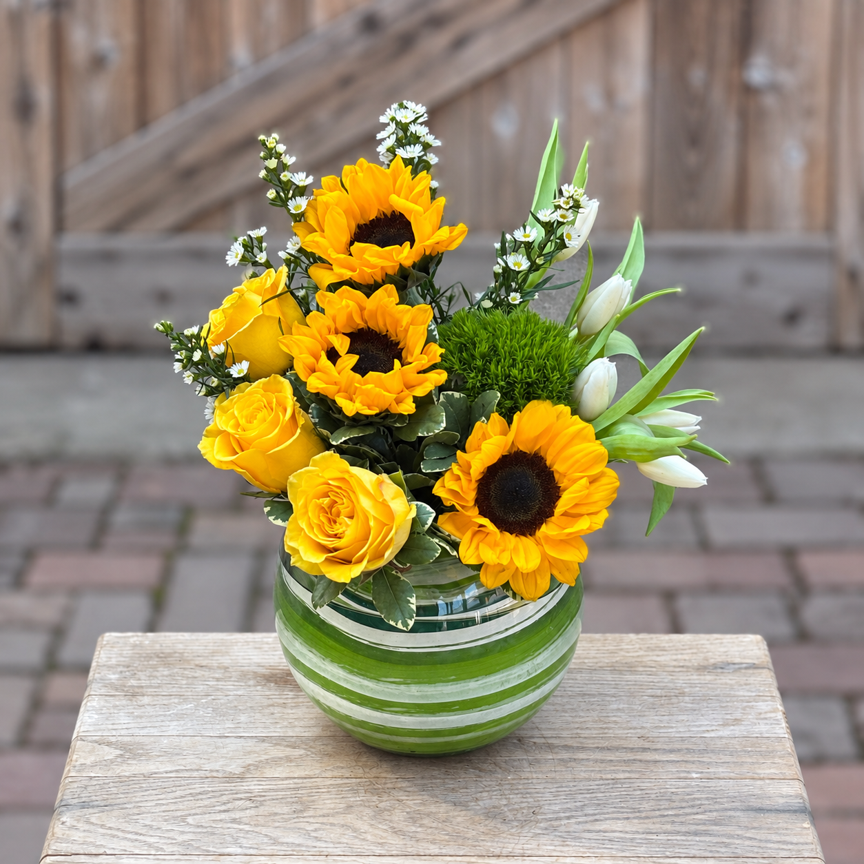 Sunflower, yellow rose and white tulip arrangement in a green glass vase from Stems Floral & More, offering flower delivery in Rockford, IL.