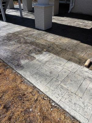 Stamped concrete walkway being sealed, next to a building, with grass and partial view of stairs.