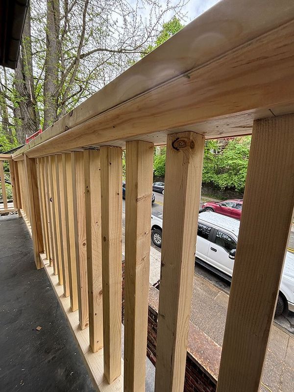 New wooden railing under construction on a porch, with vertical supports and a top rail.