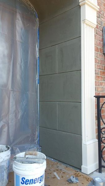 Gray stone-like wall section with white pillar beside it. Plastic sheeting and buckets present.