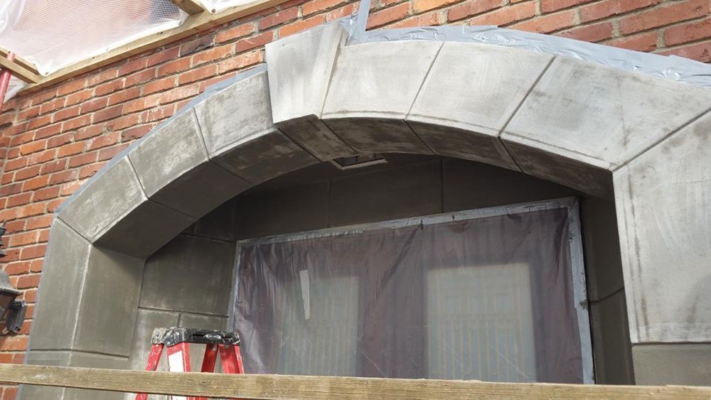Brick building with arched doorway covered in grey metal. Clear plastic sheet hangs inside.