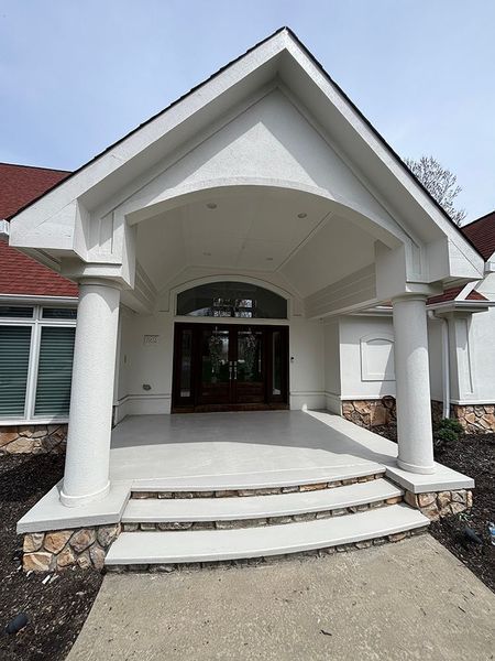 White-pillared entrance with steps, arched overhang, brown door, and tan stone accents.