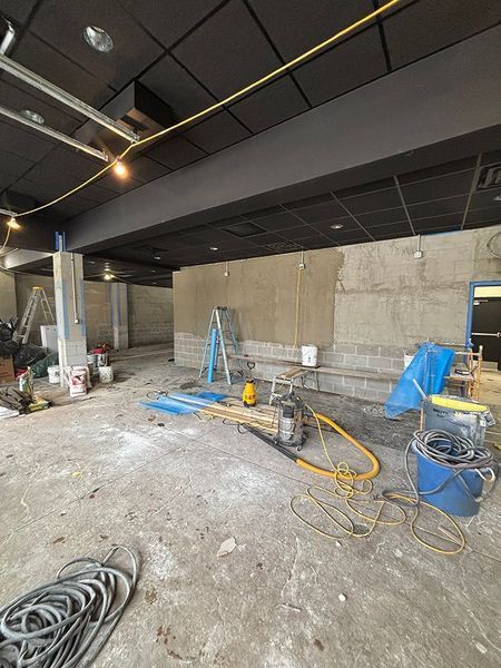 Construction site with bare walls and equipment; cement floor, black ceiling.