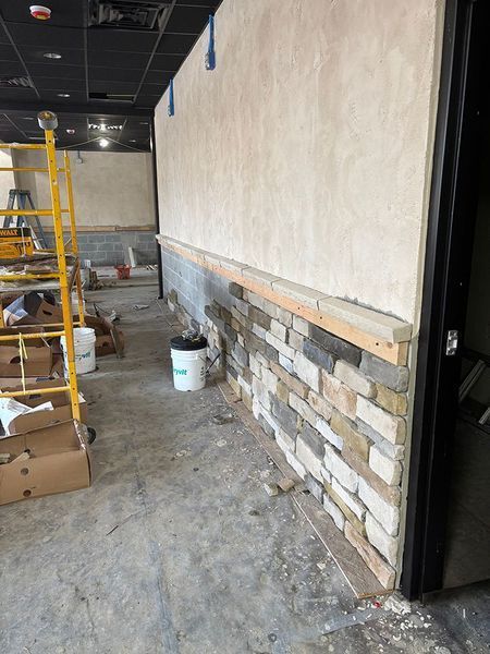 Construction in progress: wall with stacked stone veneer and stucco, with wood framing.