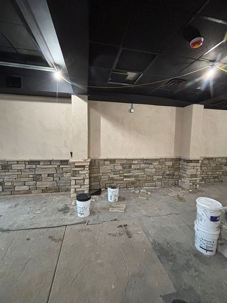 Interior under construction: stone veneer wainscoting, light walls, dark ceiling, unfinished floor, buckets.