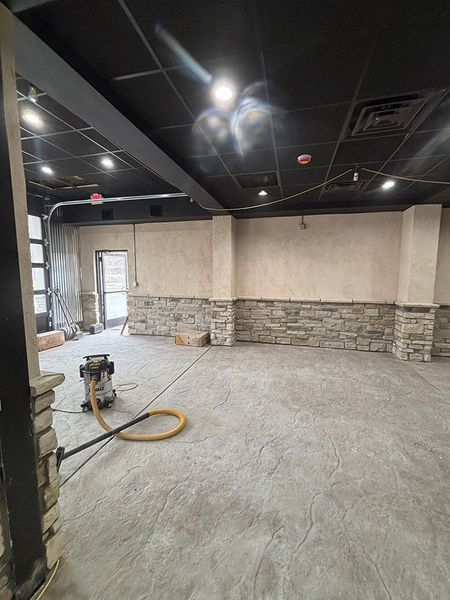 Renovated interior space with stone wall accent, gray floor, and black ceiling, during construction.