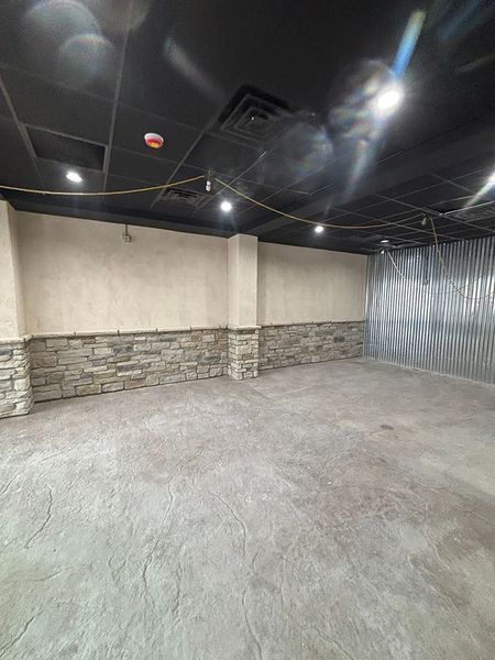 Empty room with stone and stucco walls, gray floor, black ceiling, and bright lights.