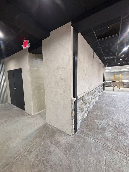 Interior view of a commercial space under construction with stone and stucco walls, concrete floor, and black ceiling.