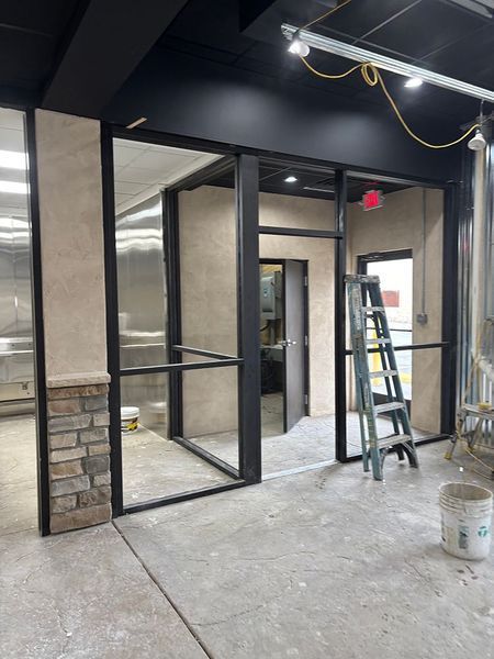 Interior shot of a commercial space under construction, showcasing glass and black metal framework with a ladder.
