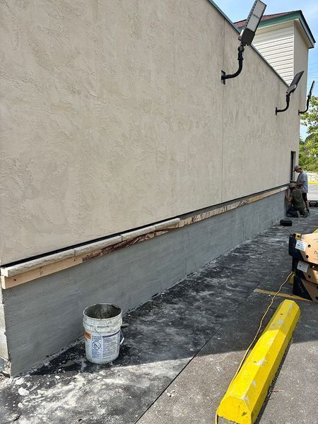 Exterior building repair; gray stucco base with new wood framing and cement; person working.