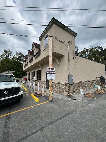 Exterior of building under renovation with stone veneer being installed. A work van is parked nearby.