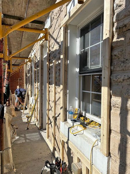 Exterior building renovation: Scaffolding, workers, window frames, stone wall.
