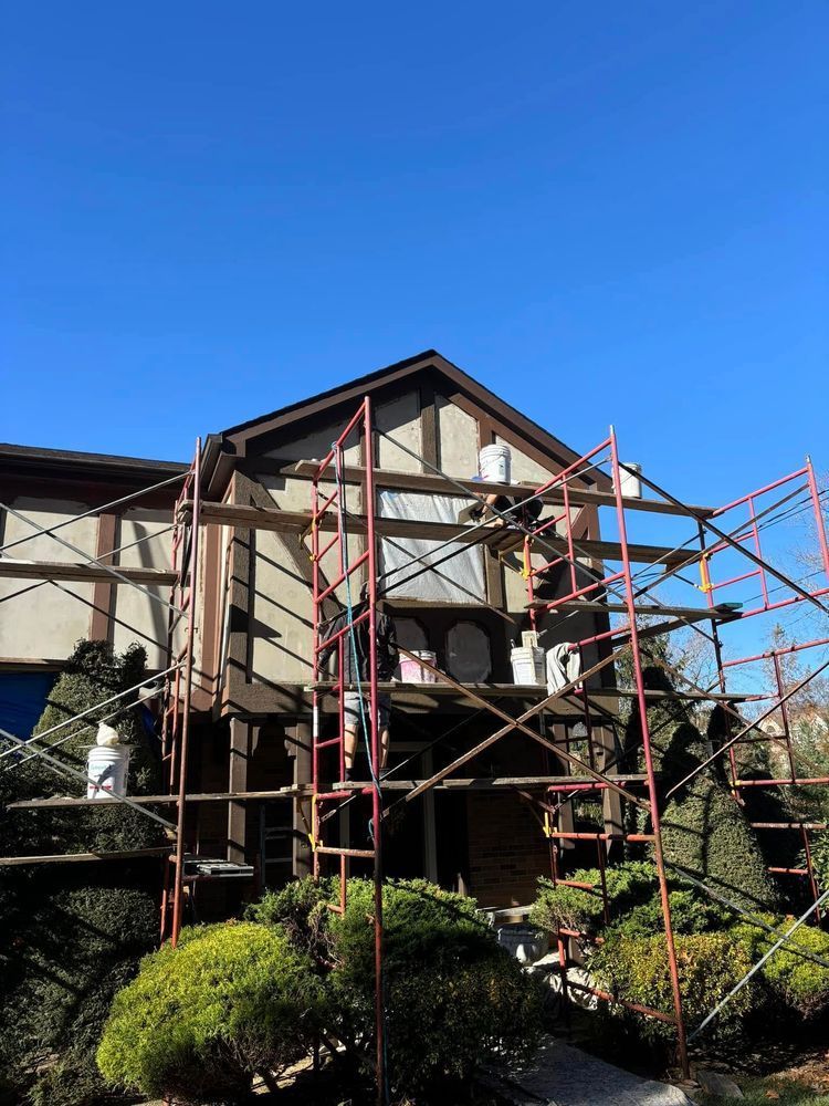 House being painted with scaffolding; brown trim, beige siding, blue sky.